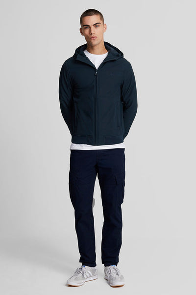 Veste de pluie bleue de LYLE & SCOTT avec capuche, portée sur un t-shirt blanc et un pantalon cargo bleu marine.