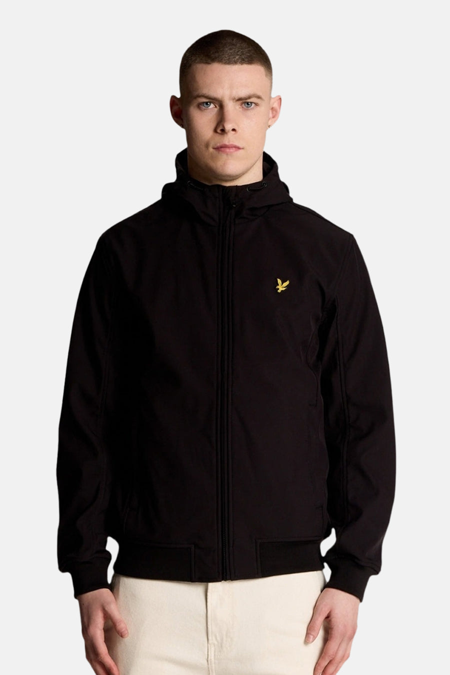 Veste de pluie noire de LYLE & SCOTT, avec capuche et fermeture éclair, portée sur un pantalon clair.