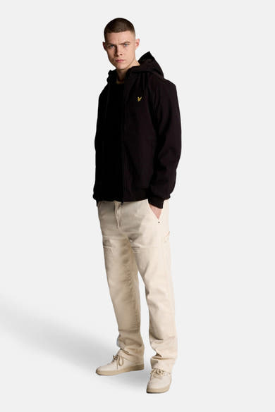 Veste de pluie noire de LYLE & SCOTT, portée avec un pantalon beige et des chaussures assorties.