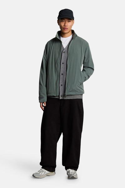 Kaki regenjas van LYLE & SCOTT, gedragen met een grijze cardigan en een wijde zwarte broek.