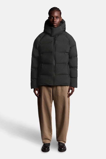 Zwarte regenjas van LYLE & SCOTT, met capuchon, gedragen met een bruine broek en zwarte schoenen.