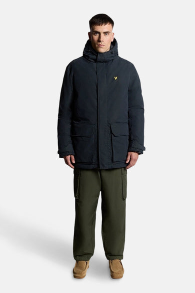 Blauwe regenjas van LYLE & SCOTT, met capuchon en opgestikte zakken, gedragen met een olijfgroene cargobroek en suède loafers.