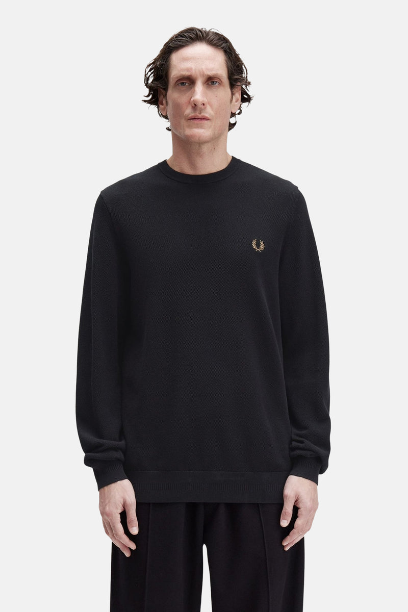 Zwarte rondehals trui van Fred Perry, versierd met een geborduurd logo op de borst, gedragen met een zwarte broek.