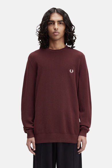 Bordeaux ronde hals trui van FRED PERRY, met geborduurd logo, gedragen over een zwarte broek.