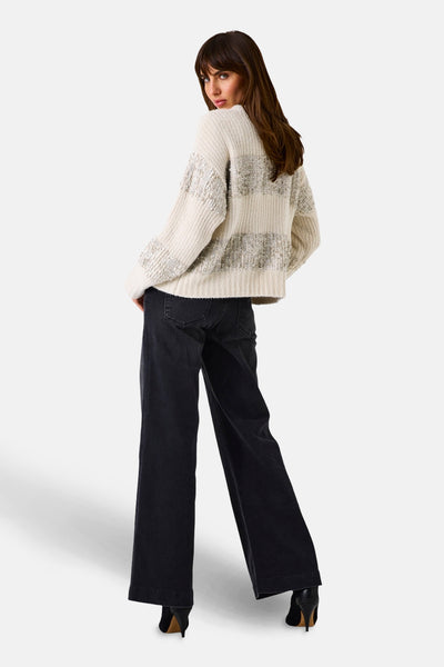 Beige ronde hals trui van GARCIA, zilveren horizontale strepen, gedragen met een zwarte jeans en zwarte hoge hakken.