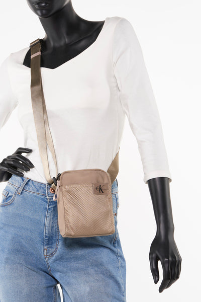 Sac à bandoulière marron de Calvin Klein, porté sur un mannequin avec jean et chemise blanche.
