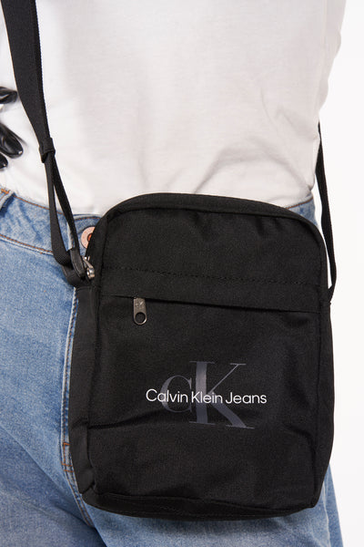 Zwarte schoudertas van Calvin Klein Jeans, gedragen met een wit T-shirt en een blauwe spijkerbroek