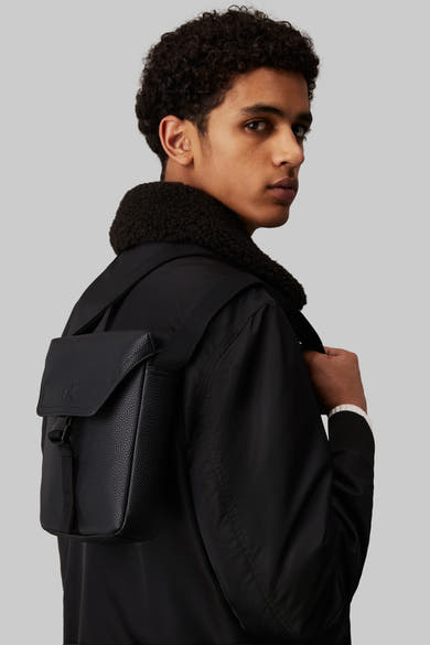 Zwarte Calvin Klein schoudertas met getextureerde flap, gedragen met een pilotenjack met imitatiebontkraag.