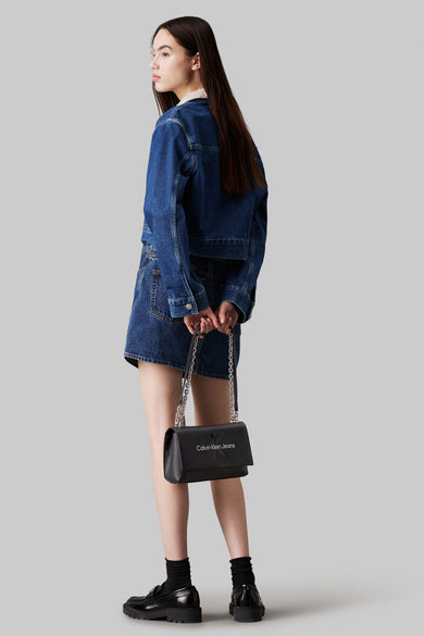 Zwarte Calvin Klein schoudertas met zilveren ketting, gedragen met een spijkeroutfit.