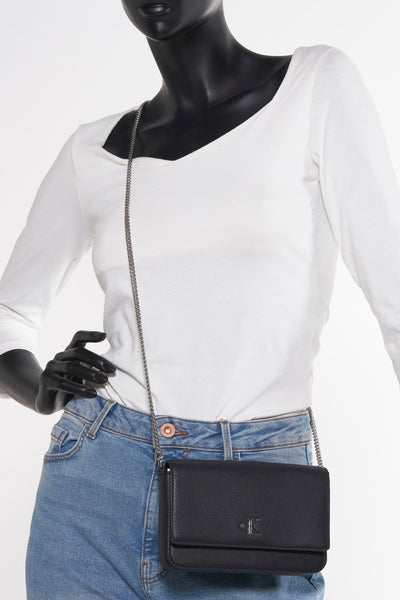 Zwarte Calvin Klein schoudertas met zilveren kettingriem, gedragen met een blauwe jeans.