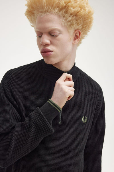 Pull noir à col montant de Fred Perry avec texture gaufrée et fermeture éclair partielle.