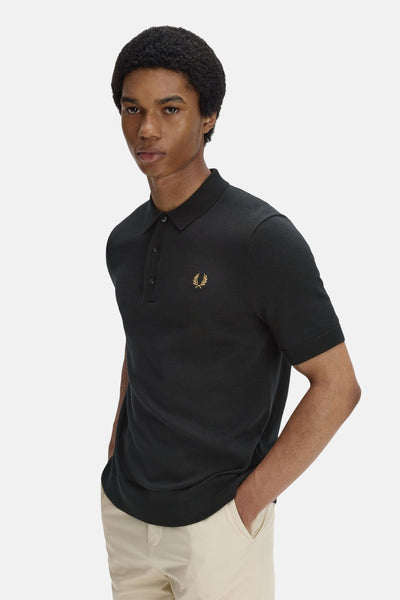 Polo noir par FRED PERRY, orné du logo distinctif, porté avec un pantalon beige décontracté.