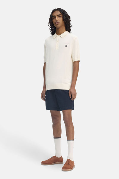 Ecru poloshirt met korte mouwen van FRED PERRY, gedragen met een marineblauwe korte broek, witte sokken en bruine schoenen.