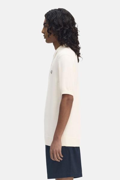 Ecru poloshirt met korte mouwen van FRED PERRY, zijwaarts gezien, gedragen met een marineblauwe korte broek.
