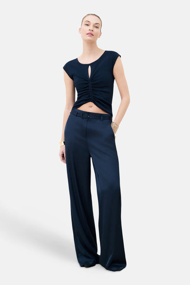 Top bleu sans manches de CAROLL, avec découpe goutte d'eau et fronces sur le devant, porté avec un pantalon taille haute.
