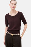 Pull brun de CAROLL à col V et manches courtes, porté avec un pantalon foncé, une ceinture claire et des accessoires dorés.