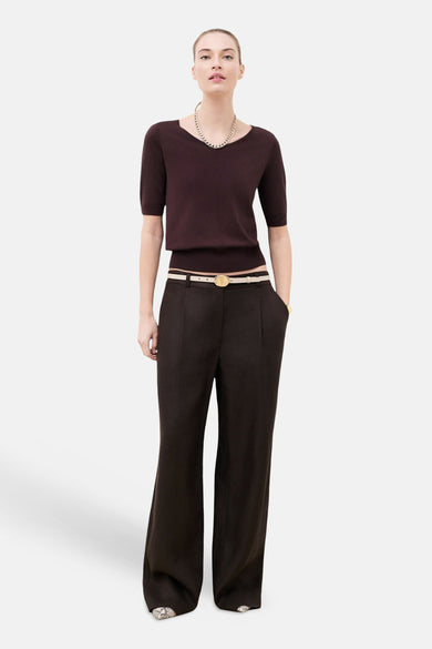 Pull col rond brun à manches courtes de CAROLL, porté avec un pantalon large, une ceinture beige et un collier doré.