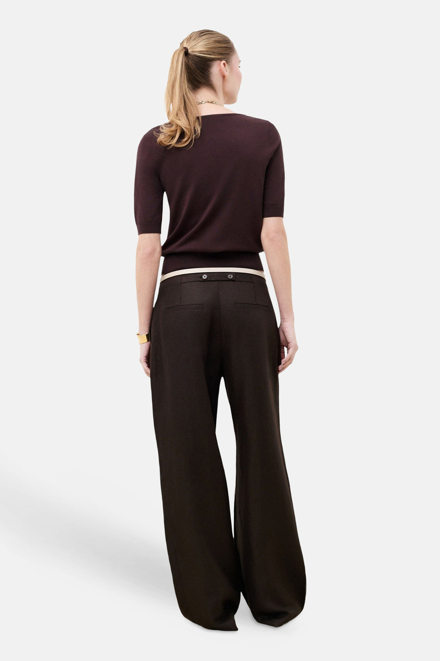 Pull col rond brun de CAROLL à manches courtes, porté au dos avec un pantalon large brun et une ceinture claire.