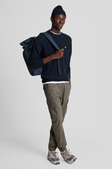 Ronde hals trui blauw van LYLE & SCOTT, gedragen met een kaki cargobroek en een marineblauwe muts.