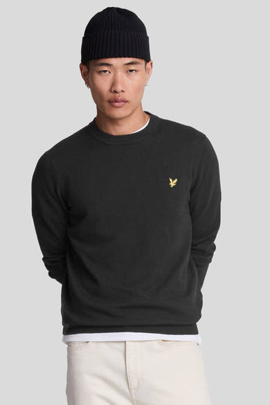 Pull à col rond noir de Lyle & Scott, porté avec un bonnet noir et un pantalon beige.