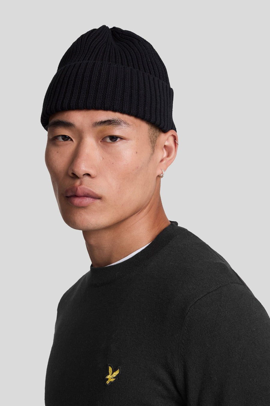 Pull à col rond noir de LYLE & SCOTT, porté avec un bonnet noir en tricot côtelé.