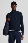 Pull à col roulé bleu de LYLE & SCOTT, porté avec un pantalon bleu marine et une casquette.