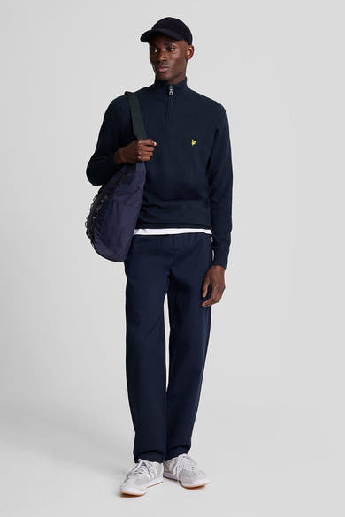 Pull à col roulé bleu marine de Lyle & Scott, porté avec un pantalon bleu marine et des chaussures de sport grises.
