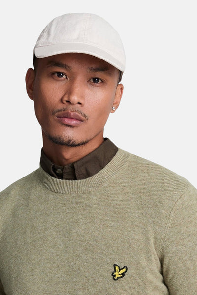 Groene trui met ronde hals van LYLE & SCOTT, gedragen met een bruin overhemd en een lichte pet.