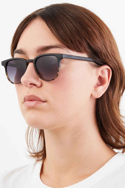 Lunettes de soleil noires par Komono, monture bicolore mouchetée et portées par une femme, vue latérale.
