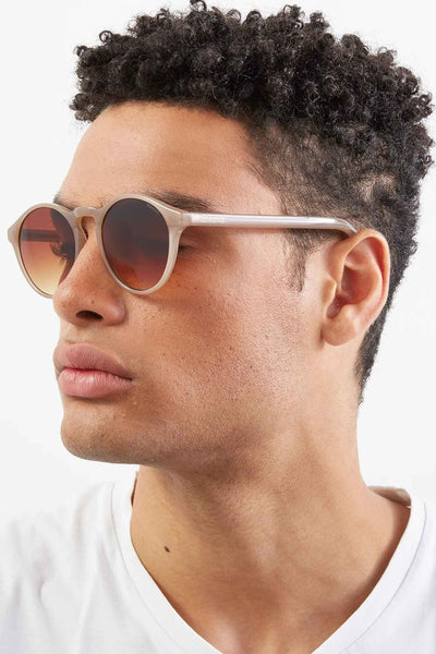 Lunettes de soleil beiges de KOMONO, avec des verres marron dégradés, portées par un homme de profil.
