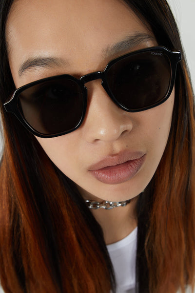 Lunettes de soleil noires de KOMONO, portées par une femme avec un collier à chaîne.