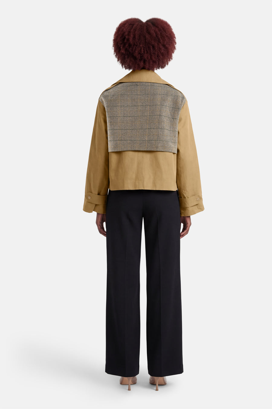 Veste courte beige de ADORE, avec empiècement à carreaux sur le haut du dos, portée avec un pantalon noir.
