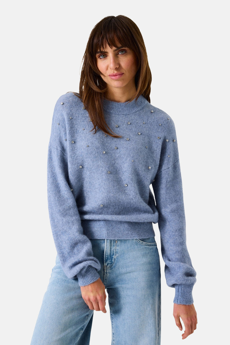 Pull bleu clair en maille duveteuse par Garcia, orné de détails brillants, porté avec un jean taille haute.
