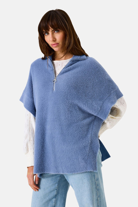 Débardeur bleu de Garcia, avec fermeture éclair et coupe poncho, porté sur un pull en dentelle.

