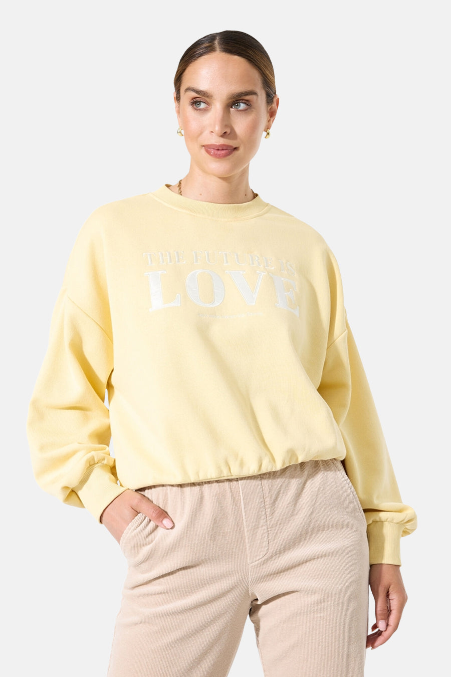Sweat-shirt jaune col rond de GARCIA, avec l'inscription "The Future is Love", porté avec un pantalon beige en velours côtelé.