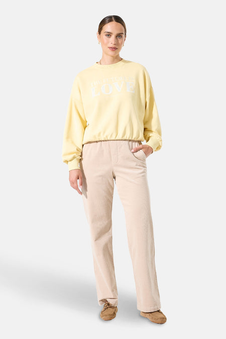 Sweat col rond jaune de GARCIA, avec l'inscription « The future is love », porté avec un pantalon beige.
