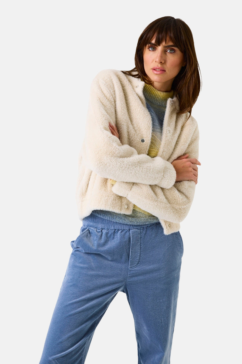 Korte gebroken witte jas van GARCIA, in getextureerd imitatiebont, gedragen over een trui met vervaagde strepen en een corduroy broek.