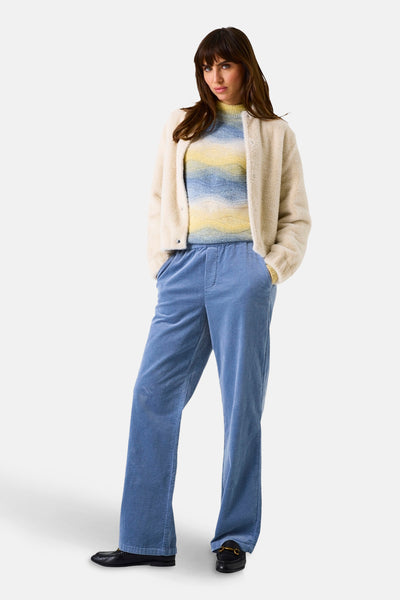 Korte gebroken witte jas van GARCIA met een pluizige textuur, gedragen over een gestreepte geel-blauwe trui, met een blauwe corduroy broek.