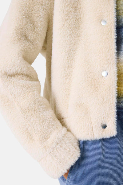 Veste courte écrue de GARCIA, texturée façon fourrure avec boutons argentés, portée sur un pull à motifs et un pantalon en velours côtelé.