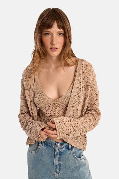 Gilet beige de Molly Bracken, en maille ajourée, porté avec un top et un jean taille haute.