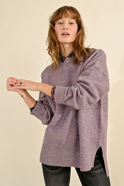 Pull à col rond violet de Molly Bracken, porté avec un chemisier à motifs floraux et un jean noir.
