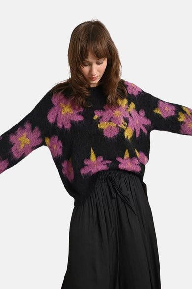 Multikleuren rondehals trui van Molly Bracken, met roze en geel bloemenpatroon op een zwarte achtergrond, gedragen met een zwarte rok.