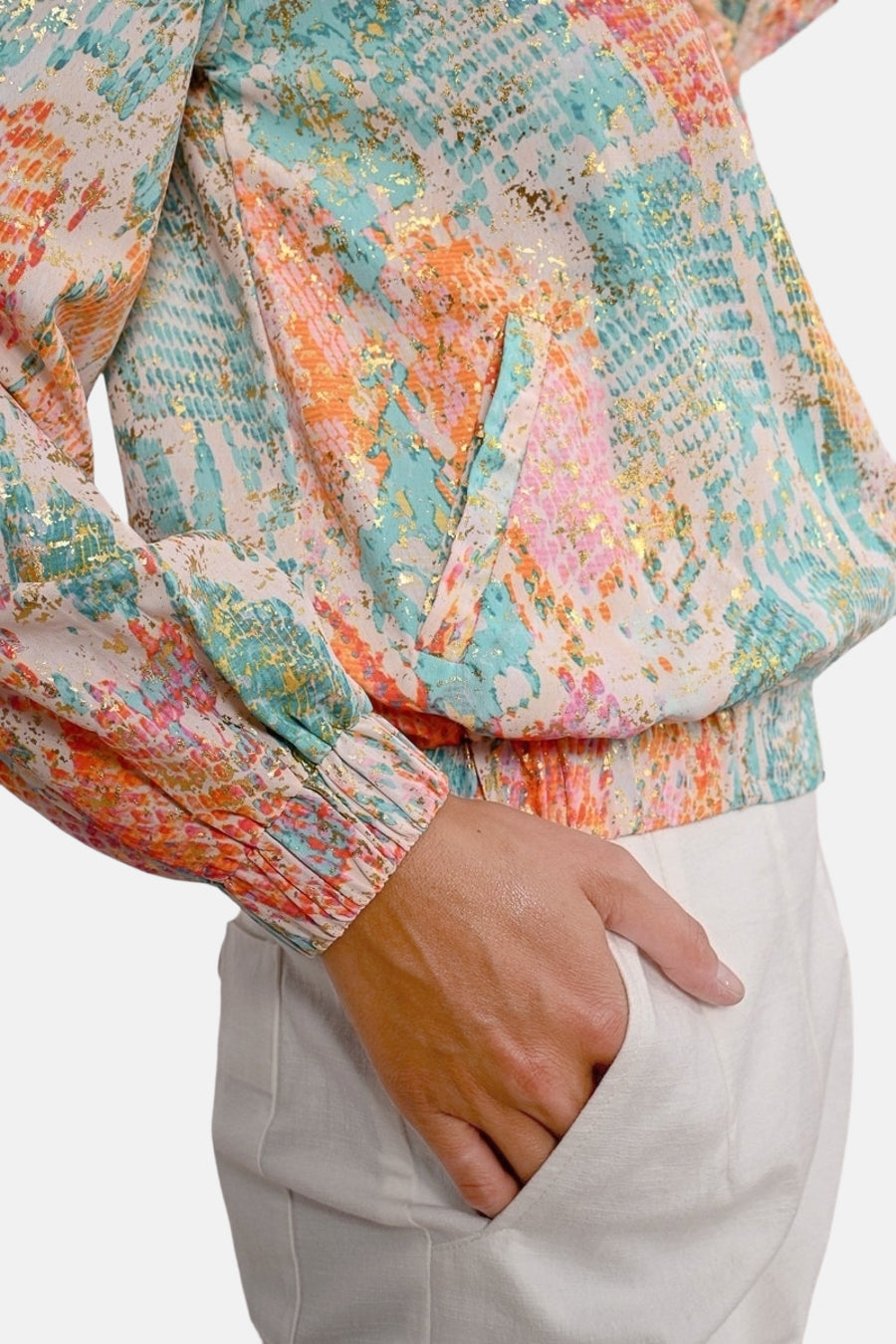 Korte meerkleurige jas van Molly Bracken, met abstracte patronen en gouden details, gedragen met een witte broek.