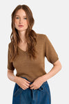 Pull col V cognac de Molly Bracken, en maille brillante, porté avec une jupe en denim bleu.