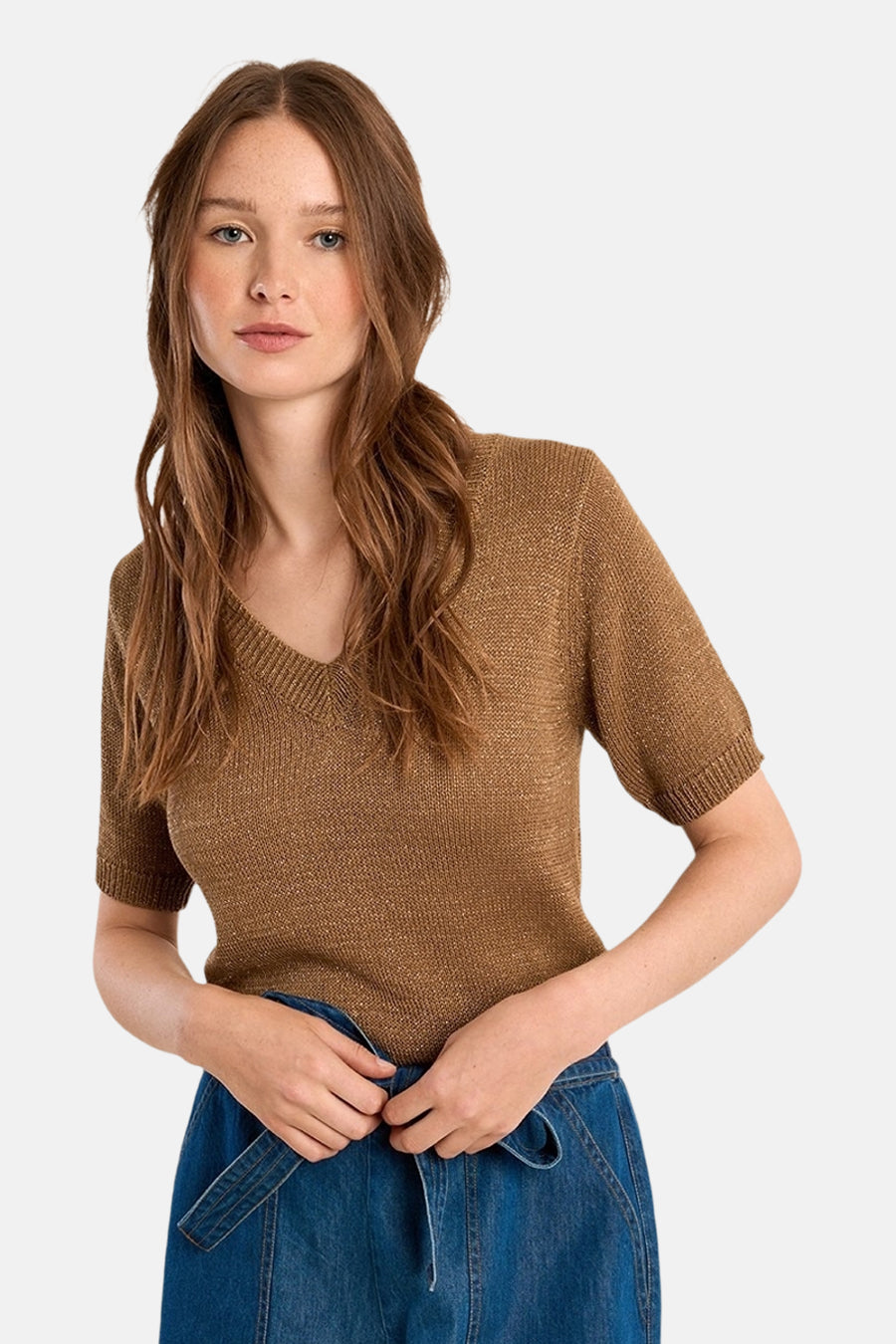Pull col V cognac de Molly Bracken, en maille brillante, porté avec une jupe en denim bleu.