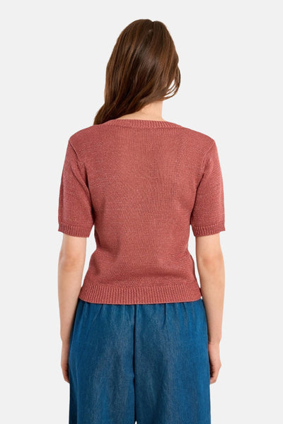 Pull col V rouge de Molly Bracken, manches courtes et texture tricotée, porté avec un pantalon ample bleu.