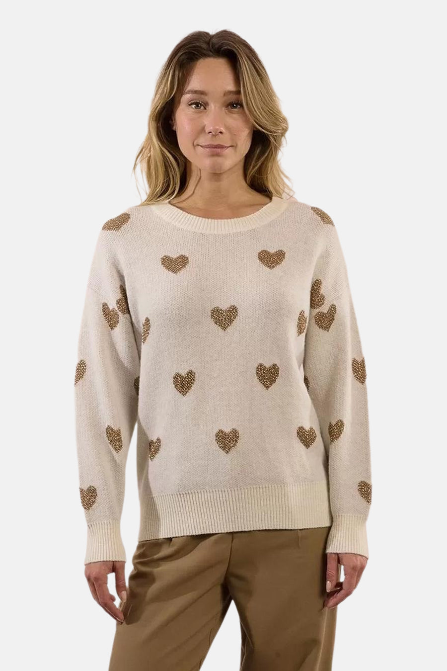 Pull écru à col rond de Molly Bracken, orné de motifs de cœurs dorés, porté avec un pantalon marron.

