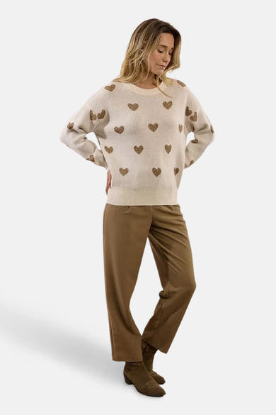Pull à col rond écru de Molly Bracken, orné de motifs de cœurs dorés, porté avec un pantalon marron et des bottines.
