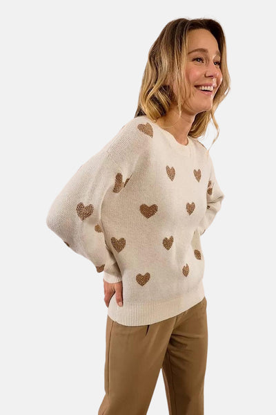 Pull à col rond écru de Molly Bracken, orné de motifs de cœurs dorés et porté avec un pantalon marron.
