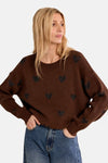 Brown O-neck sweater with black heart patterns, worn by model in side view, paired with blue jeans